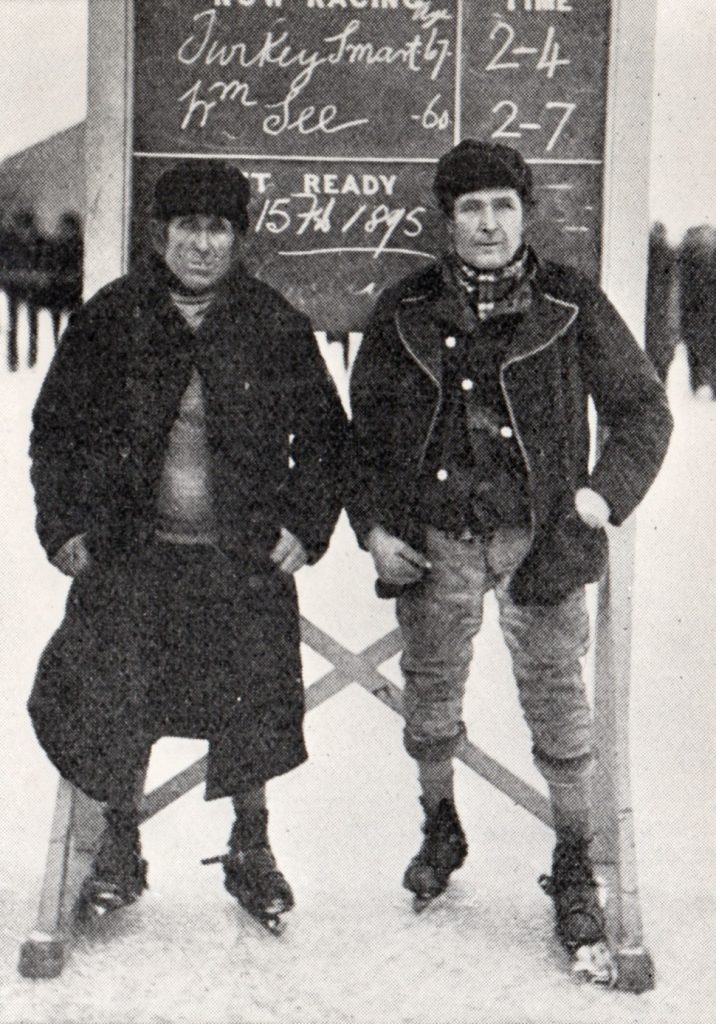 William 'Gutta Percha' See (left) and James 'Turkey' Smart (right) standing beside the scoreboard on The Moors, Littleport, 1895.